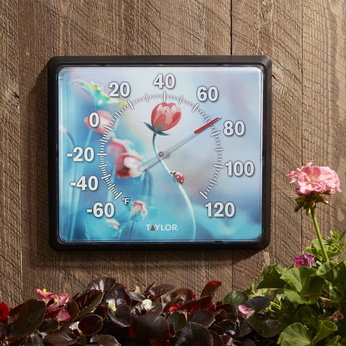Close-up of a 12x14 dial thermometer with floral design on a wood background and green numerals