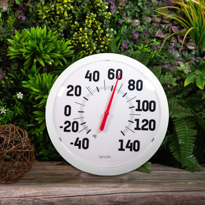 Large white round high temperature dial thermometer with bold black numerals and red needle against greenery.