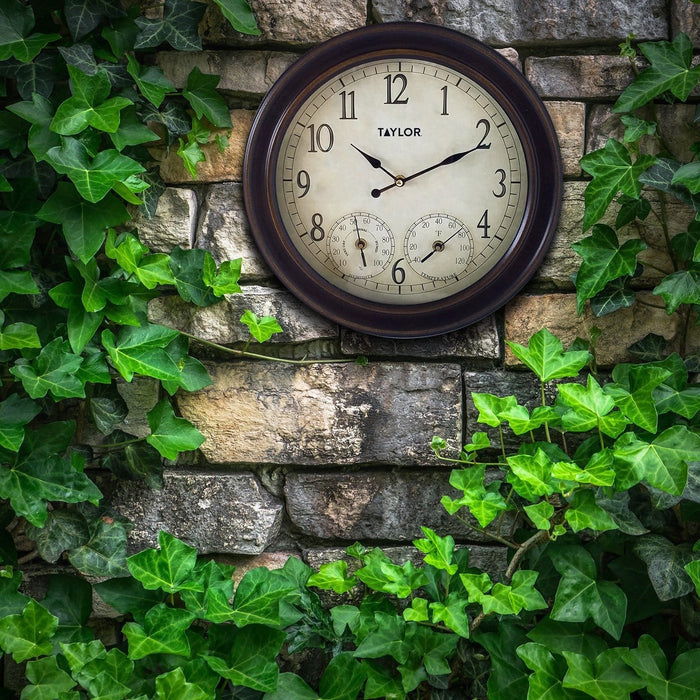 Beige faced 14 inch metal garden clock mounted on a stone wall with ivy around it