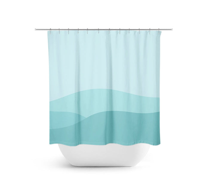 A shower curtain with an artistic interpretation of a mountain range using aqua, teal, and light blue colors. The shower curtain is hanging on a rod with a white bathtub below. This art can also be interpreted as an abstract ocean scene.