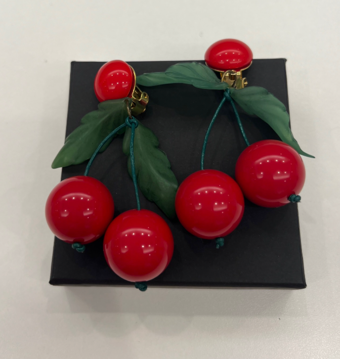 A pair of Tuckernuck Vintage Accessories clip-on earrings with three shiny red cherry-like beads and two green leaves, displayed on a black box against a white background.
