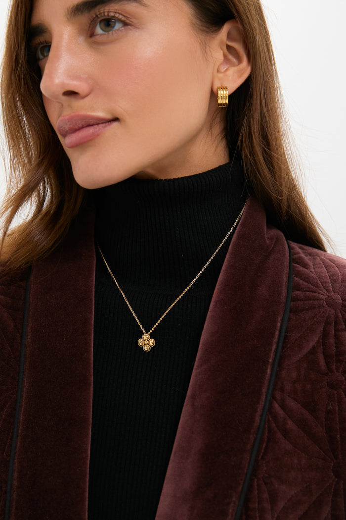 Close-up of a person wearing the Berry Clover Station Necklace in Gold; a classic, effortless piece with a clover pendant, paired with gold hoop earrings and a textured ensemble.