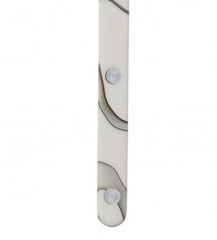 A close-up of the Sabre Bistrot Dune Butter Spreader Ivory shows its white surface with brown wavy lines, two clear round bumps resembling fasteners, and a smooth, slightly curved bottom edge—an elegant French flatware design.
