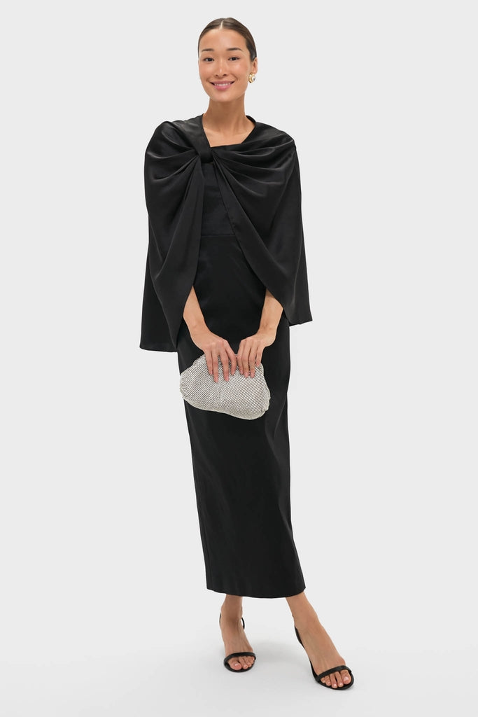 Model in the Black Satin Mountbatten Cape evening dress with a draped cape-style top, holding a crystal clutch, epitomizing classic, effortless, high-end fashion.