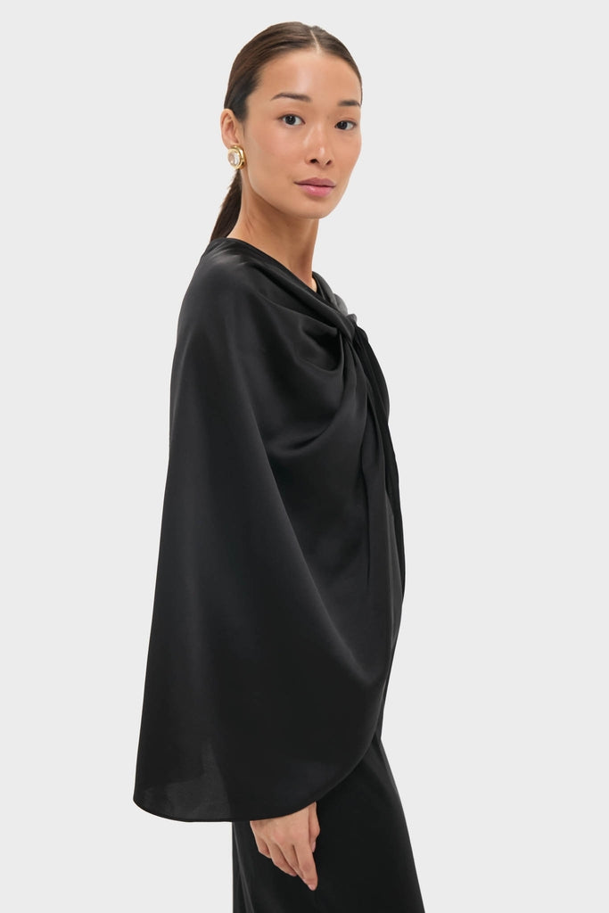 Model wearing the classic Black Satin Mountbatten Cape, featuring an effortless, high-end drape design with a gathered shoulder, styled with a large gold earring.