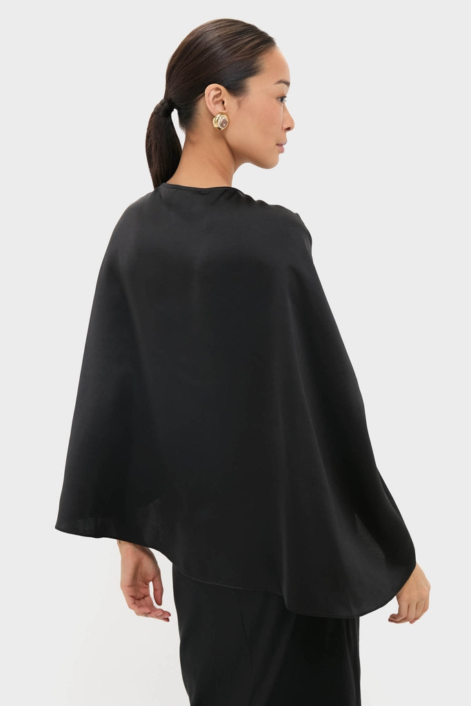 Woman in profile wearing the Black Satin Mountbatten Cape, a classic, high-end garment with effortless draping, paired with a round gold-tone earring, embodying a fun sophistication.