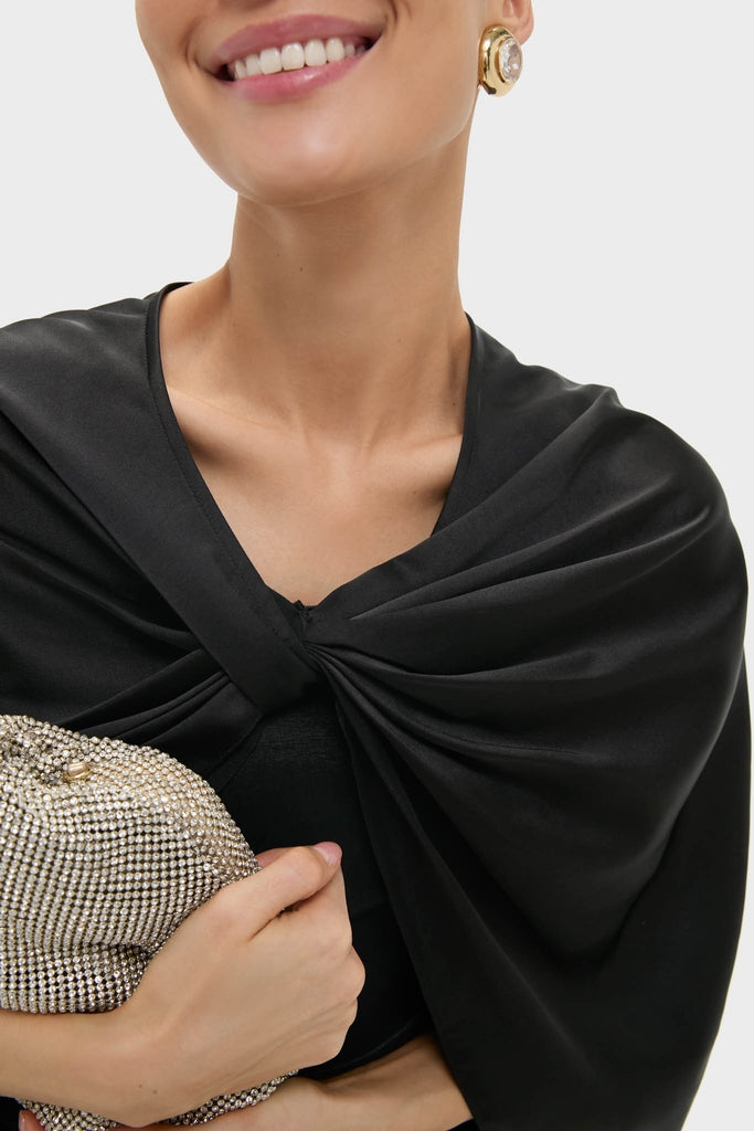 Woman wearing Black Satin Mountbatten Cape, effortlessly styled with a rhinestone clutch and vintage gold earring, showcasing classic, high-end elegance and fun textures.