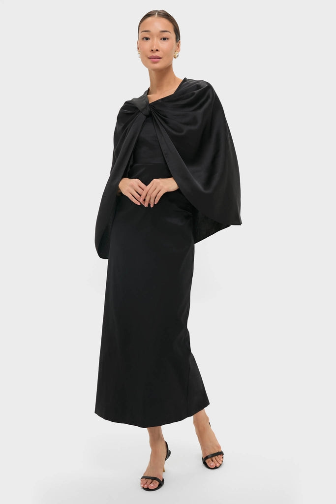 Woman wearing a classic Black Satin Mountbatten Cape, elegantly draped over a sleek black dress, embodies an effortless, high-end style with fun, matching black accessories.