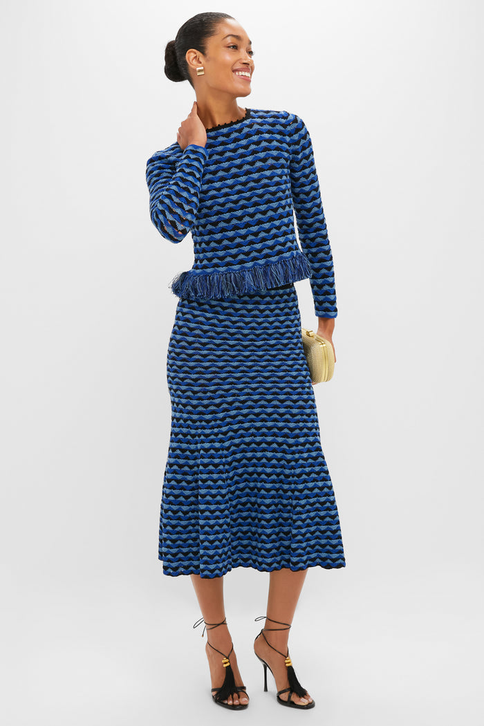 Model in Blue and Black Profundo Long Sleeve Top, featuring fringe hem, paired with matching skirt, gold clutch, and strappy heels for an effortless, high-end look.