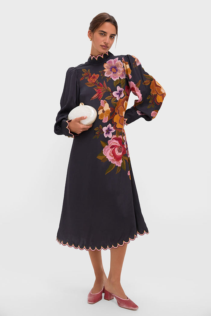 Woman in a classic floral dress showcases Tuckernuck's Blush Velvet Tilda Mules, combining effortless elegance and fun with their mule silhouette and comfortable block heel for high-end style.
