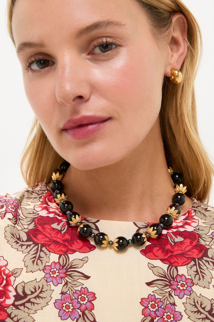 Young woman wears the Brown Tommie Necklace, a classic set of glossy black beads with gold-tone accents, paired with chunky gold hoops, exuding effortless high-end style.