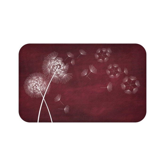 This is an image of a rectangular floor mat with rounded corners. The background of the mat mimics distressed, burgundy chalkboard. The primary graphic is a cluster of stylized dandelion seed heads on the left side. The seed heads are drawn in fine detail, and several dandelion seeds are shown floating across, suggesting a gentle breeze.
