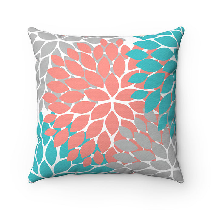 A decorative throw pillow with a floral burst design in coral, gray, and aqua colors, against a white background.