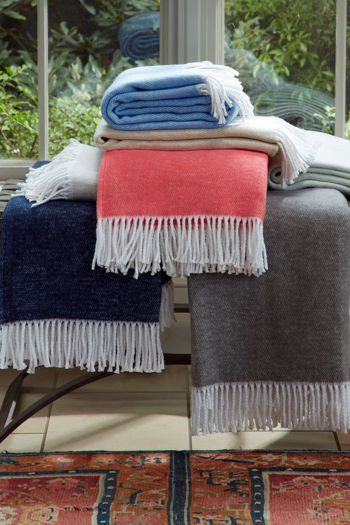 Classic Coral Pezzo Throw with fringe hem, effortlessly draped over a bench, crafted from 100% cotton. A high-end, fun accent for any lounging space.