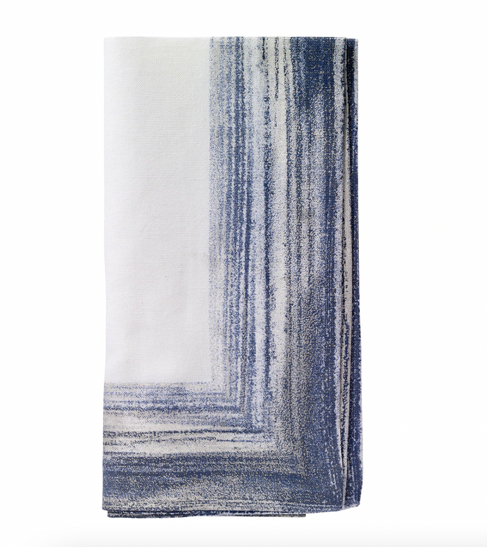 The Bodrum Cornice Napkin Navy Set of 4 features folded white cotton-linen napkins with an abstract navy and gray painterly border design on one corner, displayed against a plain white background.