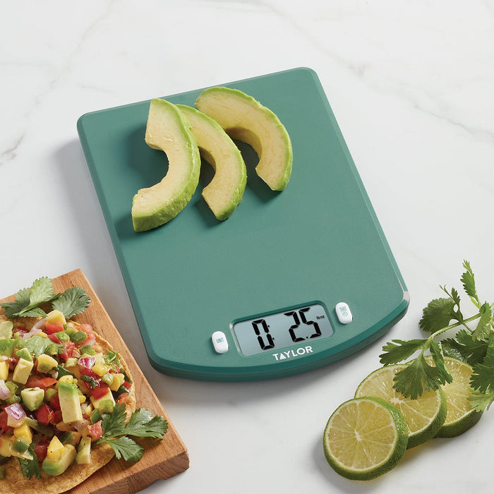 Teal Taylor digital kitchen scale with avocado slices on the platform and lime wedges nearby.