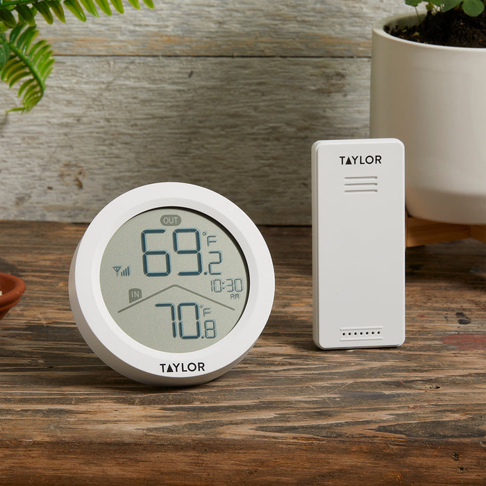 Taylor white wireless thermometer transmitter beside the round clock against a rustic wooden backdrop