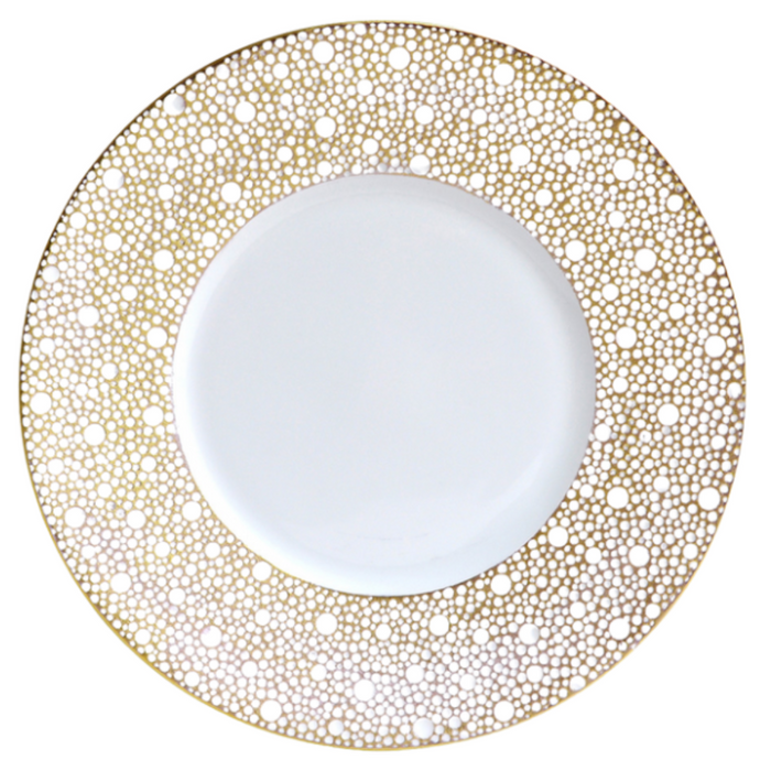 The Bernardaud Ecume Dinnerware Mordore is a round white porcelain plate with a wide rim accented by an intricate gold dotted pattern, while its center remains beautifully plain for a luxurious, elegant look.