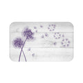 This is an image of a rectangular floor mat with rounded corners. The background of the mat mimics distressed, light gray wooden planks. The horizontal plank lines give the mat a texture and farmhouse feel. The primary graphic is a cluster of stylized dandelion seed heads (in purple) on the left side. The seed heads are drawn in fine detail, and several dandelion seeds are shown floating across, suggesting a gentle breeze.