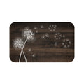 This is an image of a rectangular floor mat with rounded corners. The background of the mat mimics distressed, deep blue wooden planks. The horizontal plank lines give the mat a texture and farmhouse feel. The primary graphic is a cluster of stylized dandelion seed heads (in white) on the left side. The seed heads are drawn in white, fine detail, and several dandelion seeds are shown floating across, suggesting a gentle breeze.