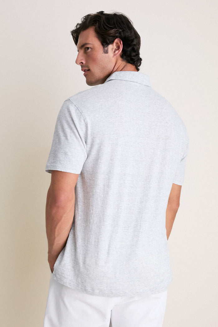 Man wearing Gale Gray Linen Sanibel Polo, stylishly casual with partial button placket, embodies Tuckernuck’s effortless, high-end style against a neutral backdrop, perfect for fun, classic adventures.