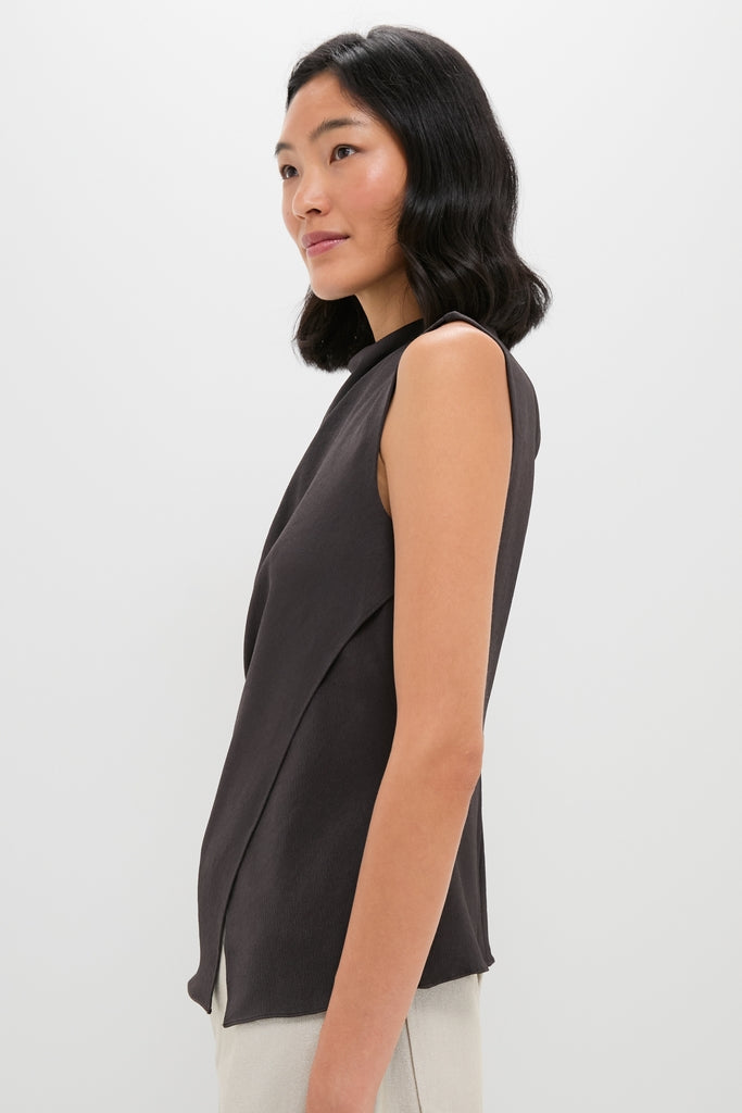 A woman stands sideways in an A.L.C. hammered crepe blouse with a gathered waist, paired with light pants, set against a plain white background.