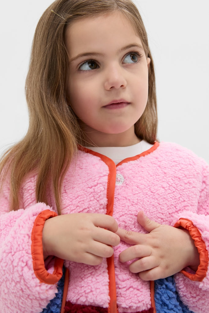Young girl in a classic, effortlessly chic Girls Ruth Jacket, featuring a pastel sherpa style with contrast piping and glitter buttons, exuding fun, high-end comfort.