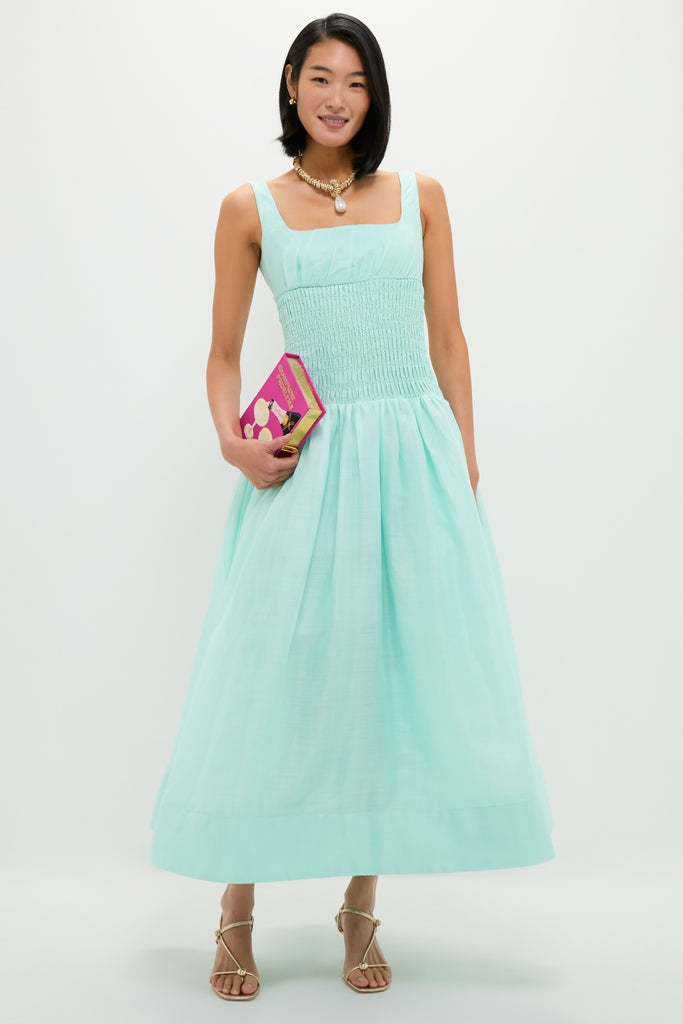 A woman models an effortless, high-end look with a classic gold pearl drop necklace, showcasing chic elegance alongside a stylish aqua dress and gold accessories.