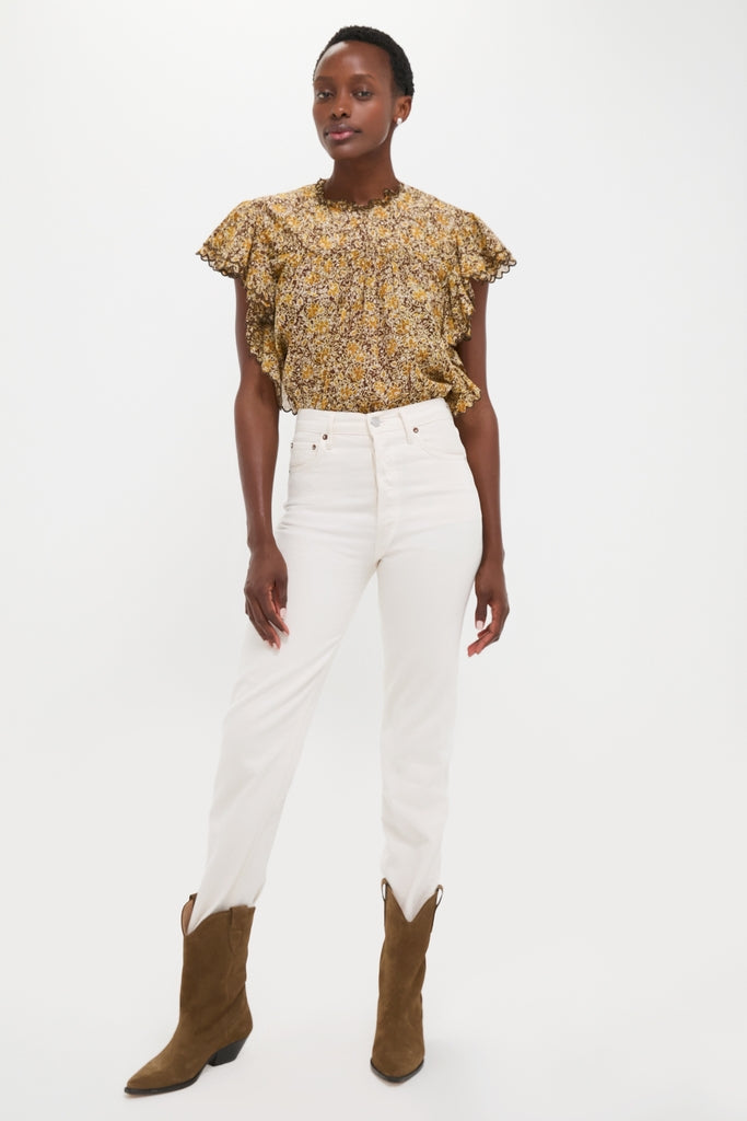 Woman models the Khaki Daliyane Top, a classic, effortless yellow-and-brown floral blouse with a ruffled yoke, paired with high-end, off-white jeans and cowboy boots.