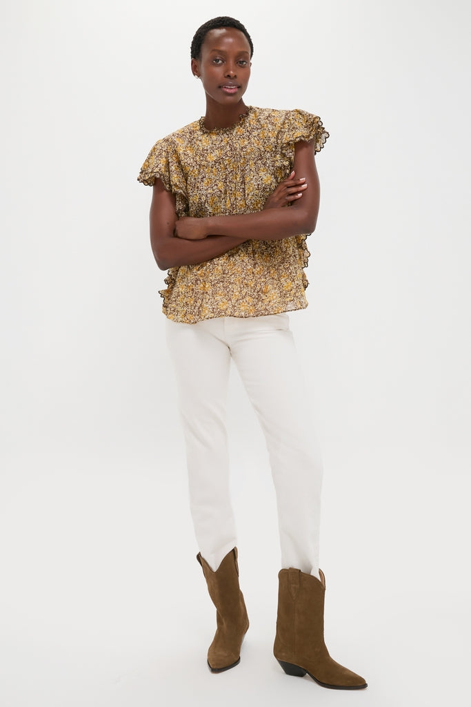 Woman models the Khaki Daliyane Top, a classic, floral-print blouse with ruffled details, paired with white jeans and brown suede cowboy boots for an effortless, high-end look.