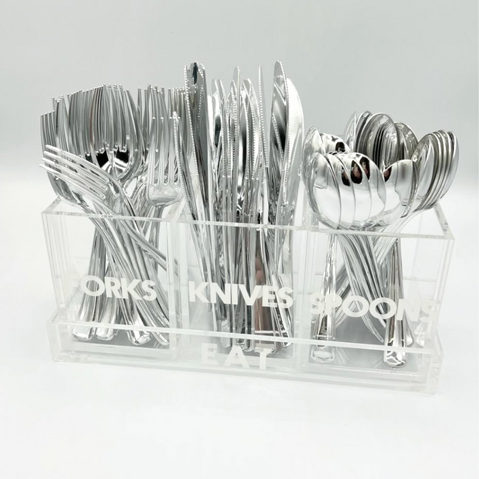 The Eye Candy Let's Eat Silverware Caddy is a clear acrylic organizer with labeled sections for forks, knives, and spoons. The words FORKS, KNIVES, SPOONS, and EAT are etched on the front.