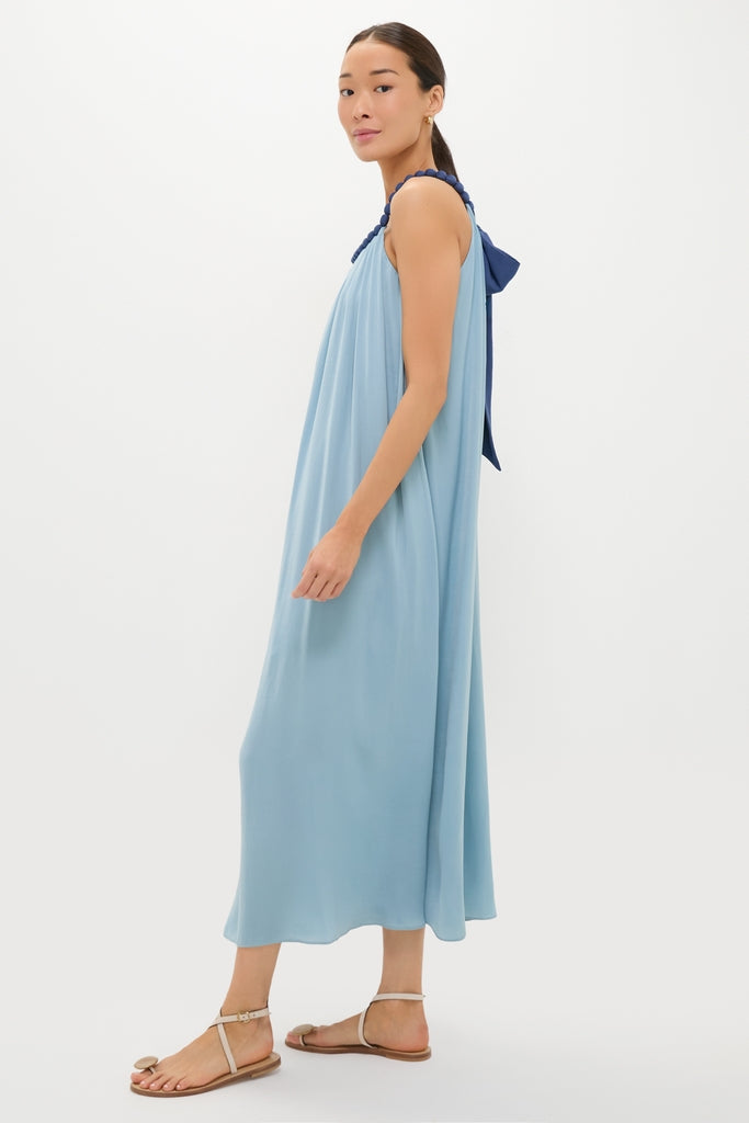 Woman in a classic, sky-blue Light Blue Chiffon Amelia Bauble Dress with navy braided straps, embodying an effortless and fun summer style, paired with beige flat sandals.