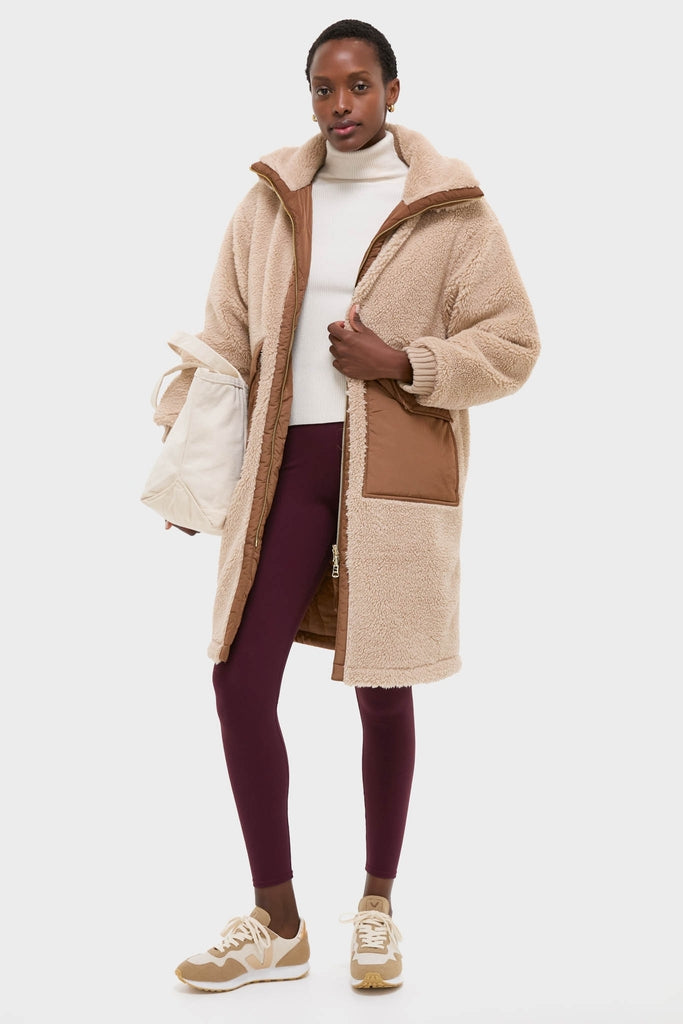 Model wearing the classic Light Taupe and Cocoa Dust Theia Reversible Coat with sherpa exterior, over an effortless cream turtleneck and plum leggings, embodying high-end, fun style.