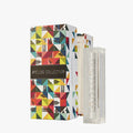 A vibrant geometric box labeled Apeloig Collection sits beside a Modern Acrylic Mezuzah Case 4.5", containing a white decorative candle marked "INSTRUCTIONS," blending contemporary design with tradition.