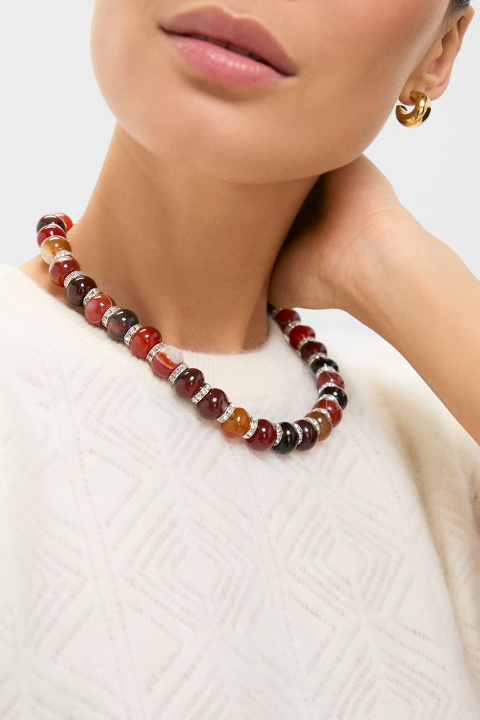 A classic and effortless Multi Thea Necklace featuring chunky, polished stones separated by metallic rings, paired with a cream sweater and gold hoop earring for a fun, high-end look.