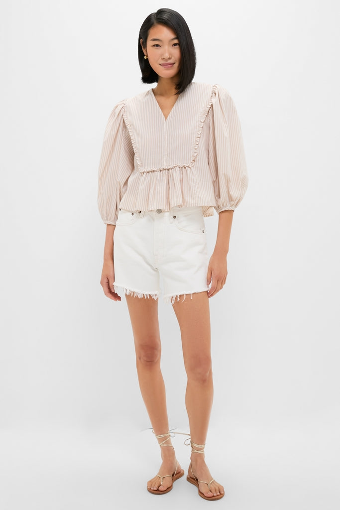Young woman models the Natural Stripe Stevie Blouse, showcasing a classic, effortless style with its pinstripe pattern, ruffle trim, and voluminous three-quarter sleeves.