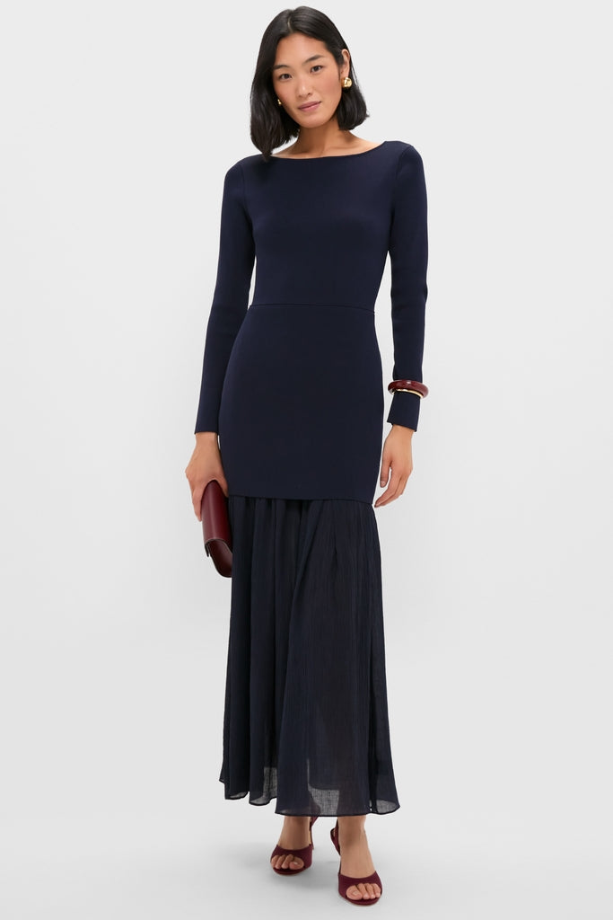 Woman models the classic Navy Gemma Mix-Media Dress, featuring an effortless knit top, drop waist, and sheer skirt. Accessorized with gold hoops, burgundy clutch, and heels.