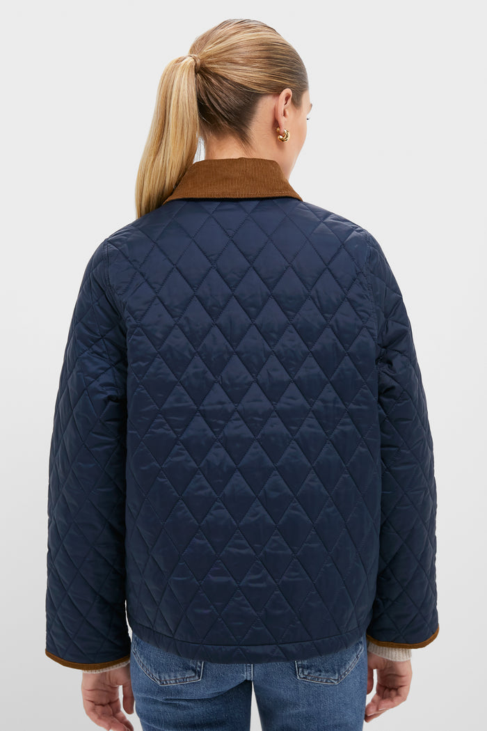 A woman with blond hair in a ponytail is seen from behind wearing a Barbour jacket with a brown collar, set against a plain light background.