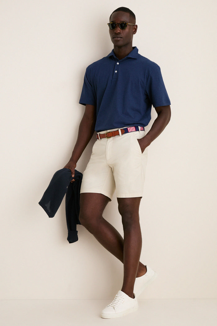 Model in navy Ryles Crown Flex Cotton Polo, classic cutaway collar, with beige chino shorts and red-white belt, embodying effortless, high-end style.
