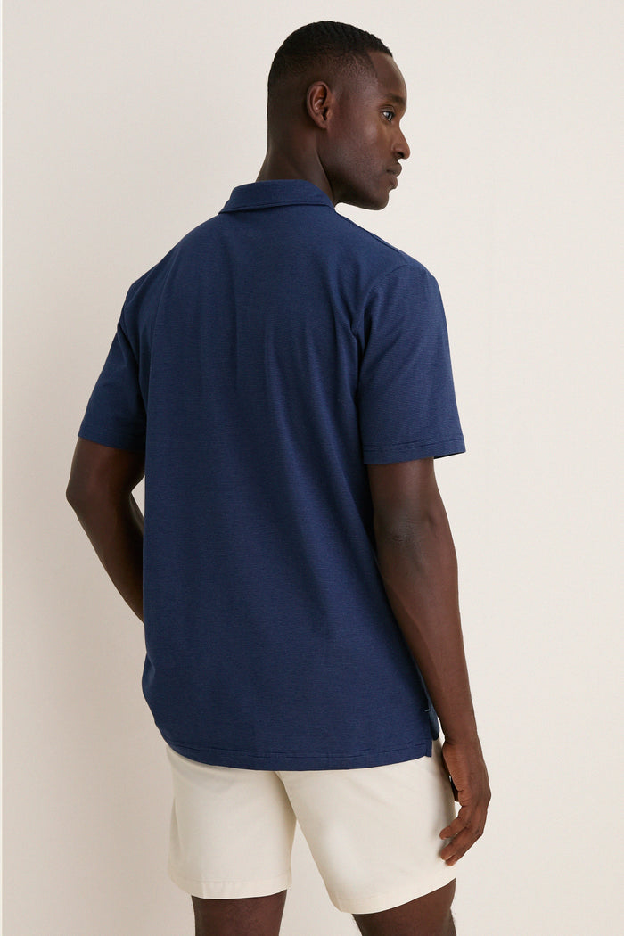 Man in classic Navy Ryles Crown Flex Cotton Polo with cutaway collar and beige shorts, exudes effortless style and fun against a simple off-white backdrop.