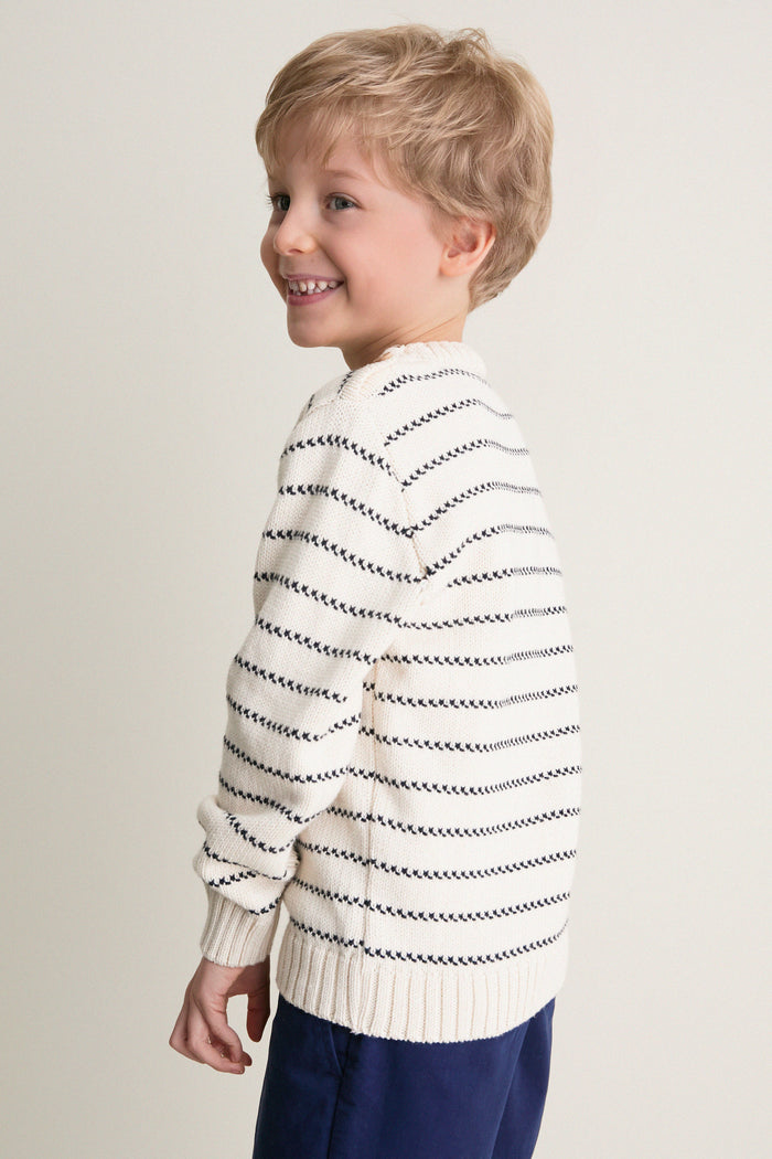 Young boy in profile wearing the Navy Stripe Raya Cotton Jumper, showcasing classic navy intarsia stripes, ribbed trims, and handcrafted wooden shoulder buttons; an effortless, fun, high-end staple.