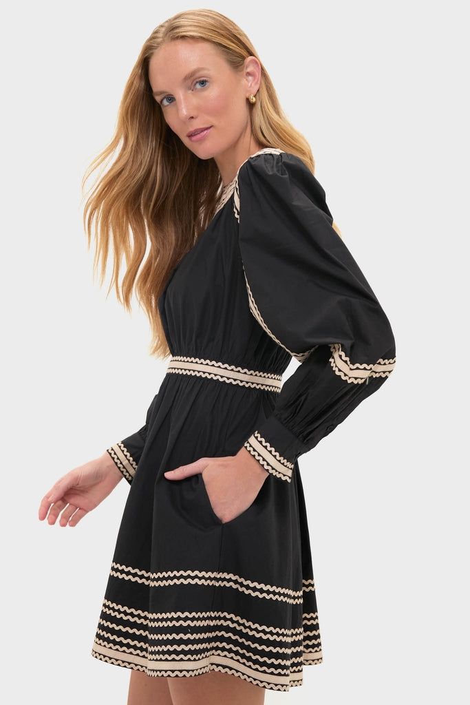 Model wearing the classic Noir Fiora Mini Dress with cream wavy trim, featuring puffed sleeves, a fitted waist, and side pockets, exuding effortless, high-end style.