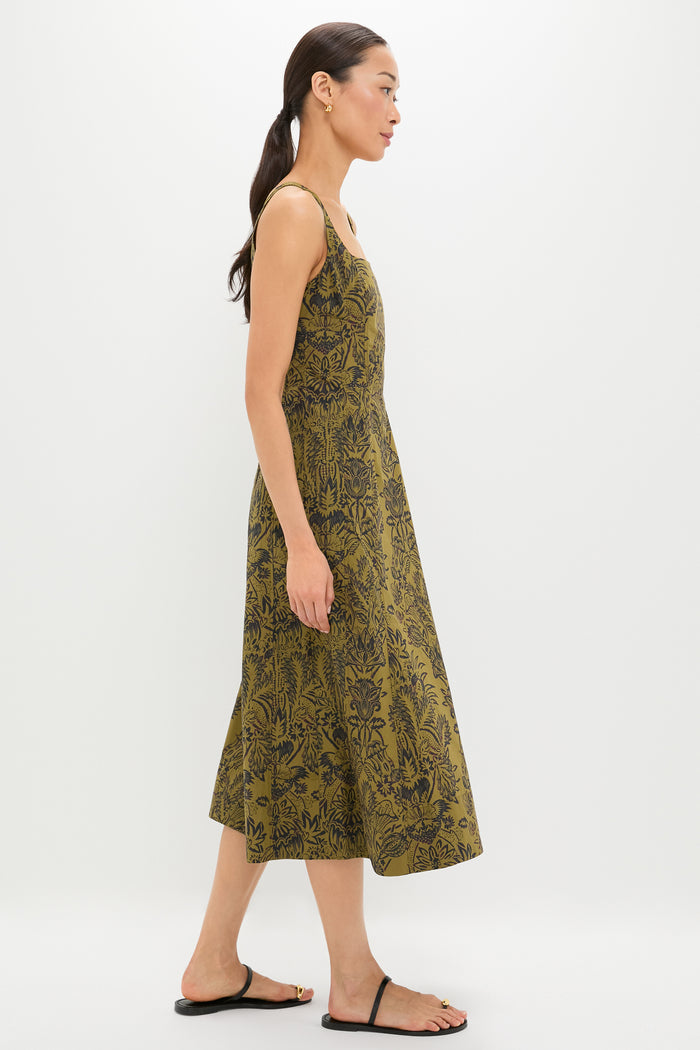 Woman wearing the Olive Flora Natali Dress, a sleeveless midi with an all-over black botanical print, embodies classic, effortless style. Paired with black sandals and gold hoops for a high-end look.