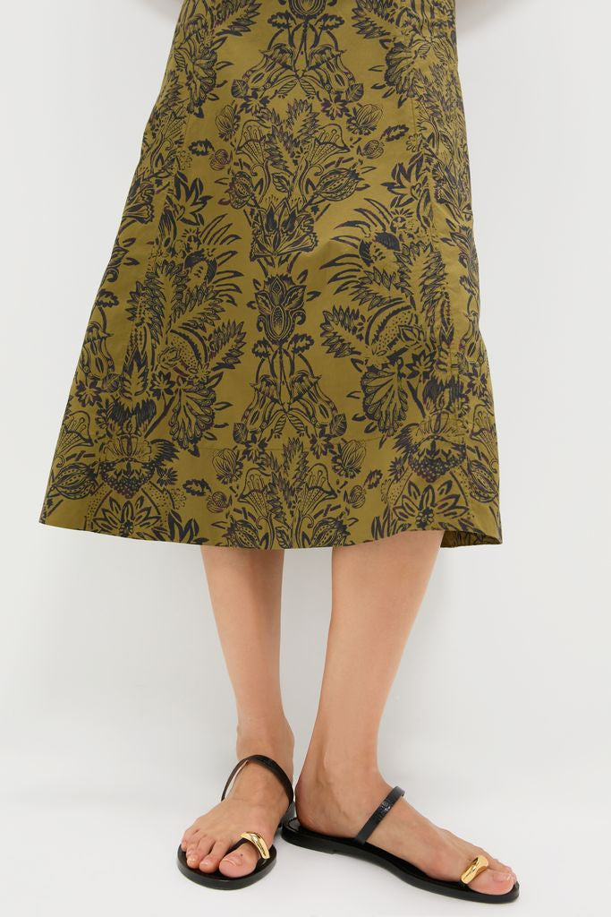 Person wearing the classic Olive Flora Natali Dress, featuring an intricate floral print, paired with effortless black sandals embellished with high-end gold-tone accents, embodying fun and confidence.