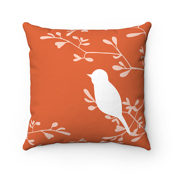 A square decorative throw pillow with an orange background, featuring a white love bird perched on a branch with off-white branches in the background.