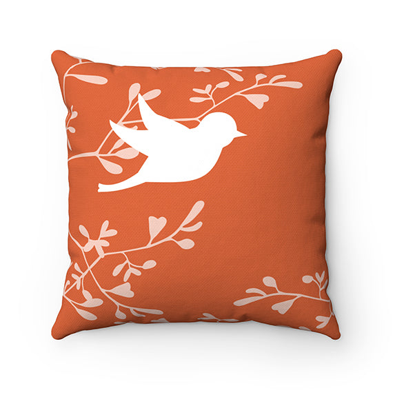 Square pillow with an orange background and off-white branches with leaves and a white silhouette love bird in a flying pose.