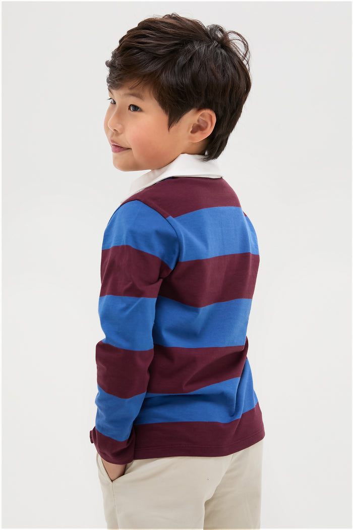 Young boy wearing the classic Petrol Blue Stripe Tijo Long Sleeve Boy Rugby Shirt, effortlessly styled for a fun and high-end look with its vintage preppy design.