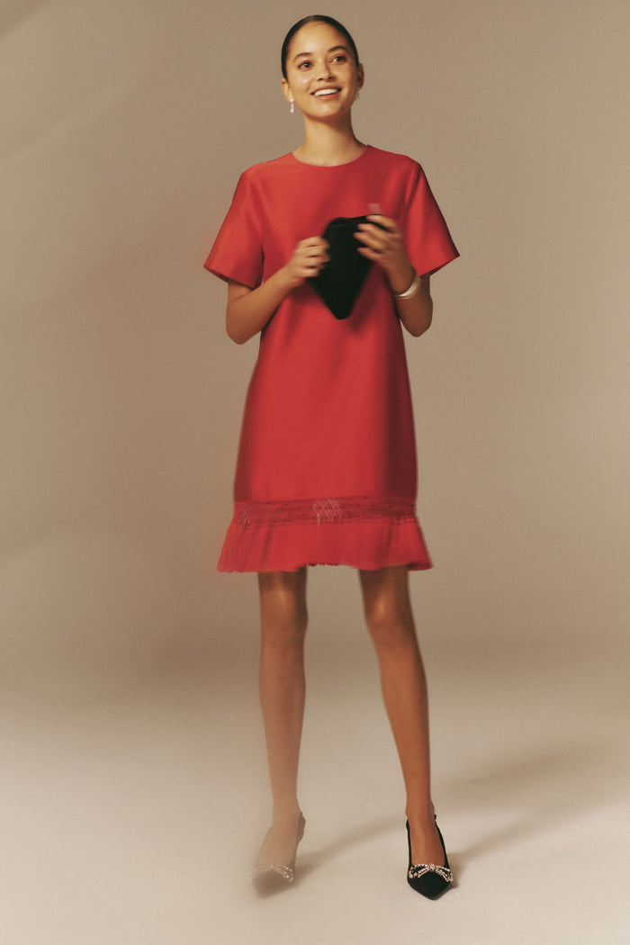 Young woman in Red Dupioni Tassel Downing Dress, holding a black clutch, wearing rhinestone-embellished heels, embodying classic, effortless style for festive, high-end occasions.