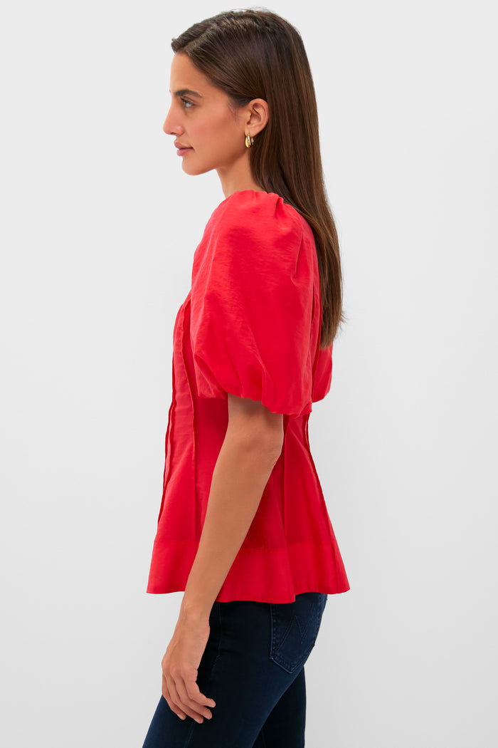 Woman in Ruby Taffeta Annalise Blouse, featuring classic puff sleeves and flared hem, paired effortlessly with dark jeans, embodies fun, high-end style.