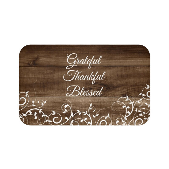 A rectangular brown memory foam mat with the text 'Grateful Thankful Blessed' printed on it, featuring a floral pattern around the edges.